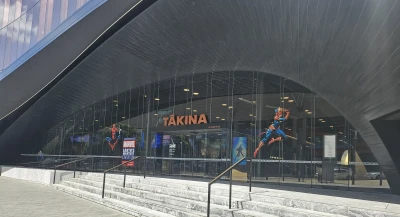 At the entrance of Tākina Convention Centre, concrete stairs lead up to a set of glass doors in a half circle frame adorned with captivating Marvel-themed attractions.