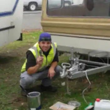 John sports his bright yellow hi-viz jacket as he kneels by a trailer towbar.