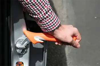 An orange handy bar is inserted into a car door latch, providing a stable support handle to assist with exiting the vehicle.