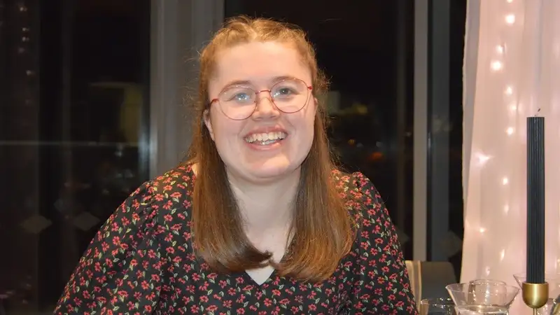 Libby is a European young girl with shoulder length brown hair. She wears red framed glasses.