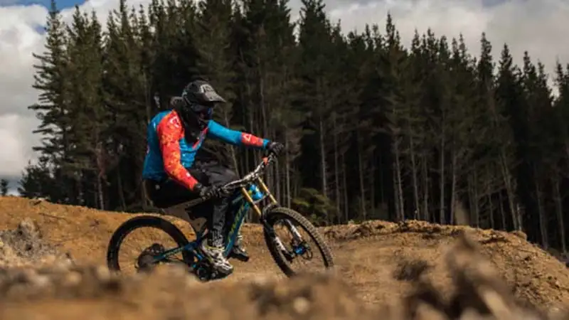 Liam is sporting his biking gears with helmet, boots, gloves, pants and blue shirt as he bikes down a track.