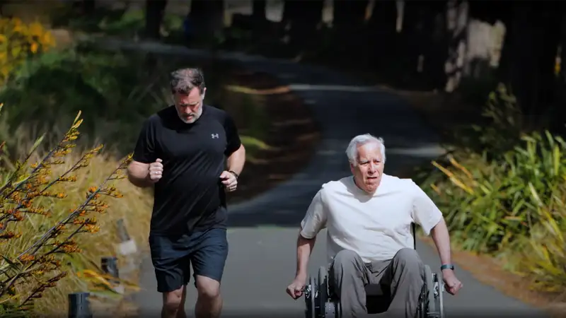 Rory and a runner a racing against each other on a wide footpath. Rory is using the OctalWheels wheelchair.