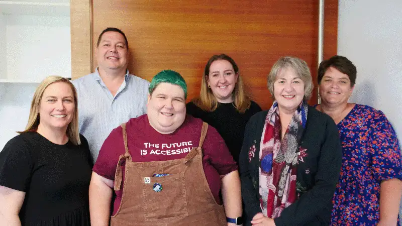 Enable New Zealand and Firstport staff are grouped with People First staff standing in front of a wooden door.