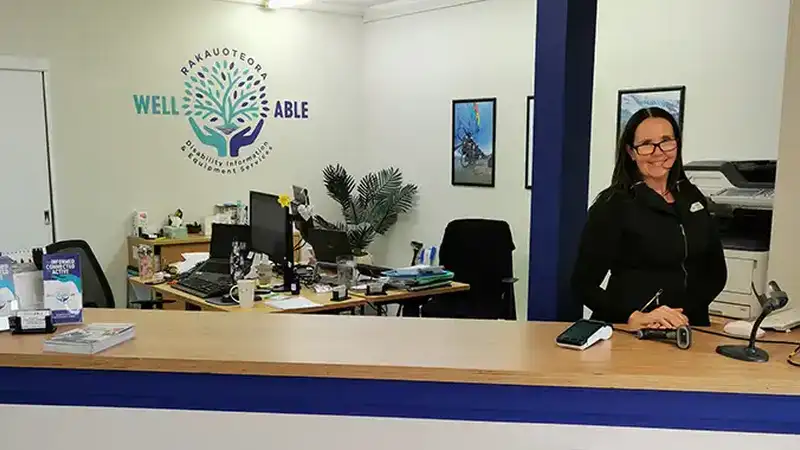 The WellABle office is brightly lit, with their logo prominently displayed in the center of the wall behind the computers. Maria, their information advisor, is doing an excellent job at the front desk.